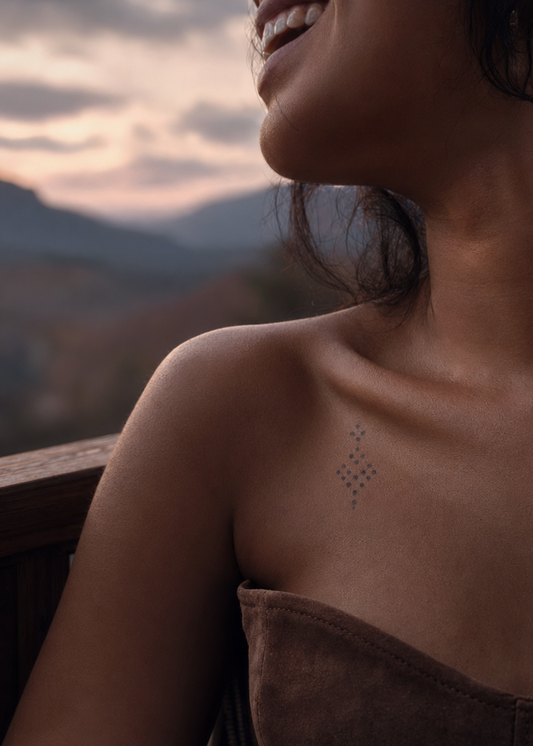 Boucle de Tulum. delicate diamond pendant ornament, dotted linework, suspended point above and below, collarbone, behind the ear line near base of neck, cloudy twilight, pastel sky reflected on skin.